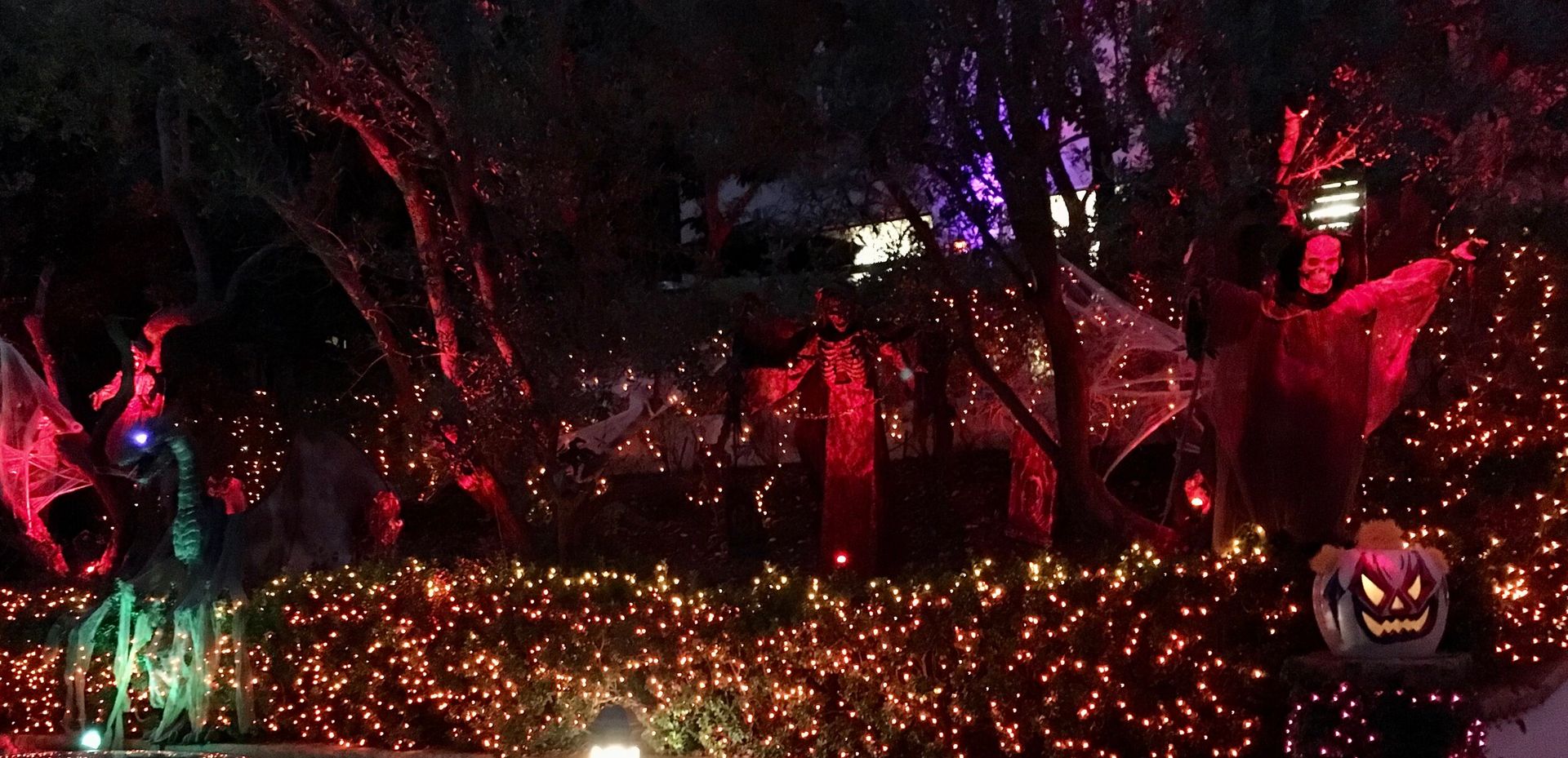A garden at night with red-lit reaper figures and glowing jack-o’-lanterns