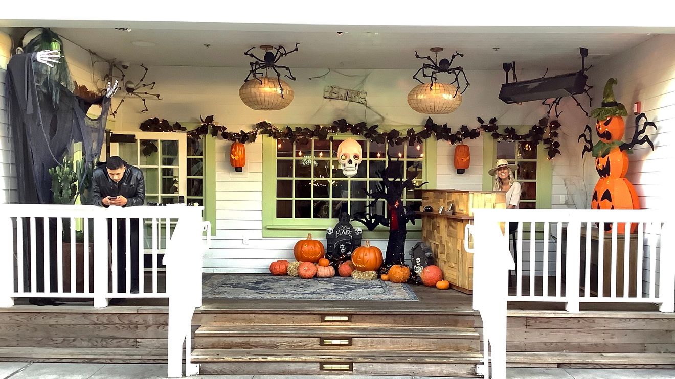 A porch decorated for Halloween with giant hanging spiders, jack-o’-lanterns and a lit BEWARE sign